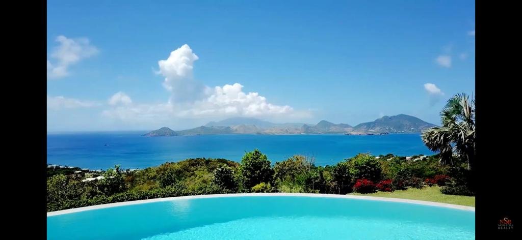 17 Degrees North Realtors, stunning ocean view with infinity pool, lush gardens, and mountain backdrop, specializing in luxury real estate in Evis for discerning buyers and investors.