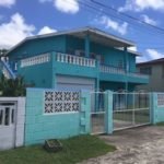 Bright turquoise two-story house with balcony and gated yard in a tropical neighborhood. Perfect for seaside living or investment property in Evis, showcasing Caribbean-style luxury.