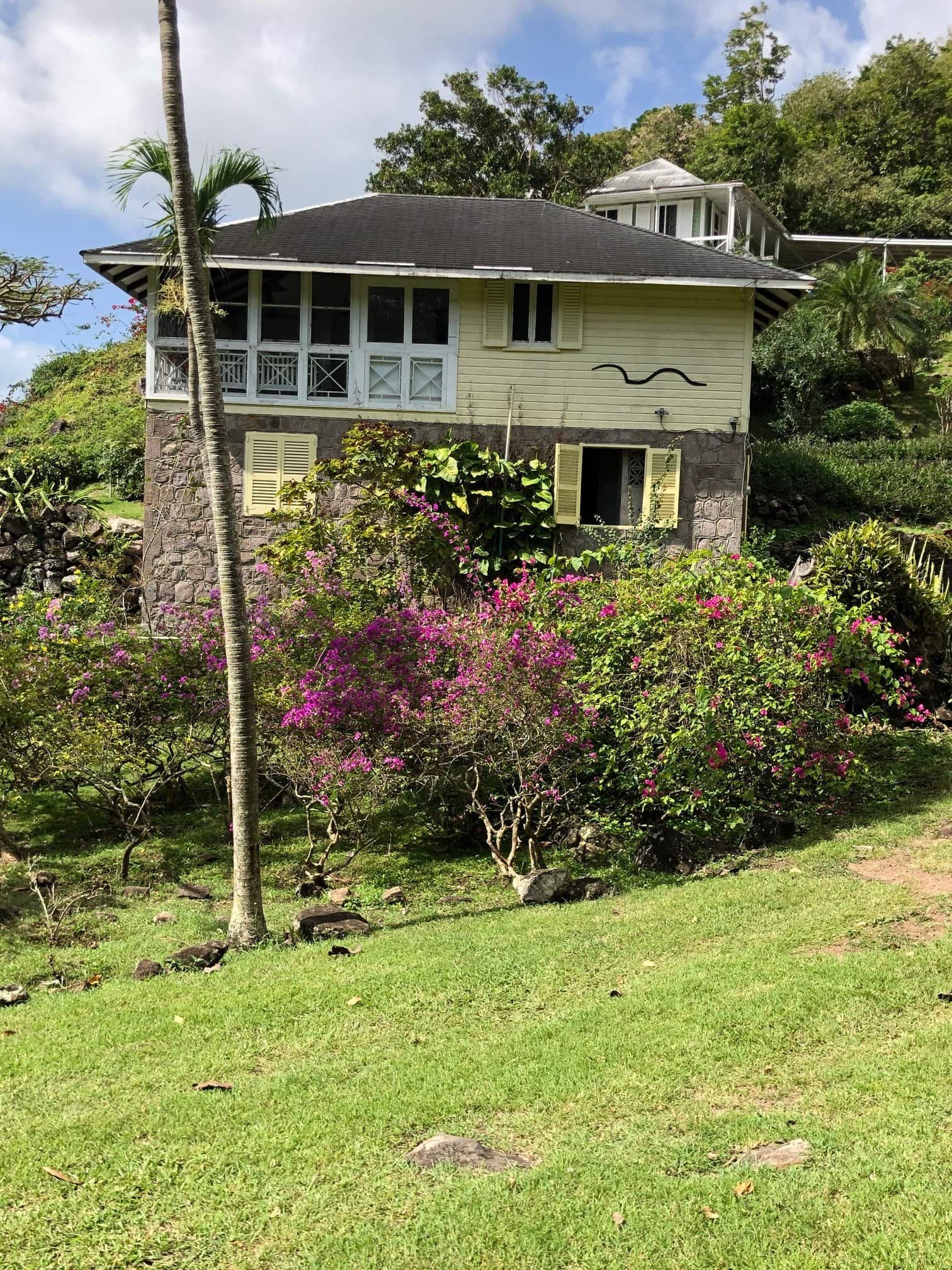 Charming hillside home with lush tropical landscaping and vibrant pink bougainvillea, showcasing a cozy residence with ocean views, perfect for buyers seeking a serene and scenic island retreat.