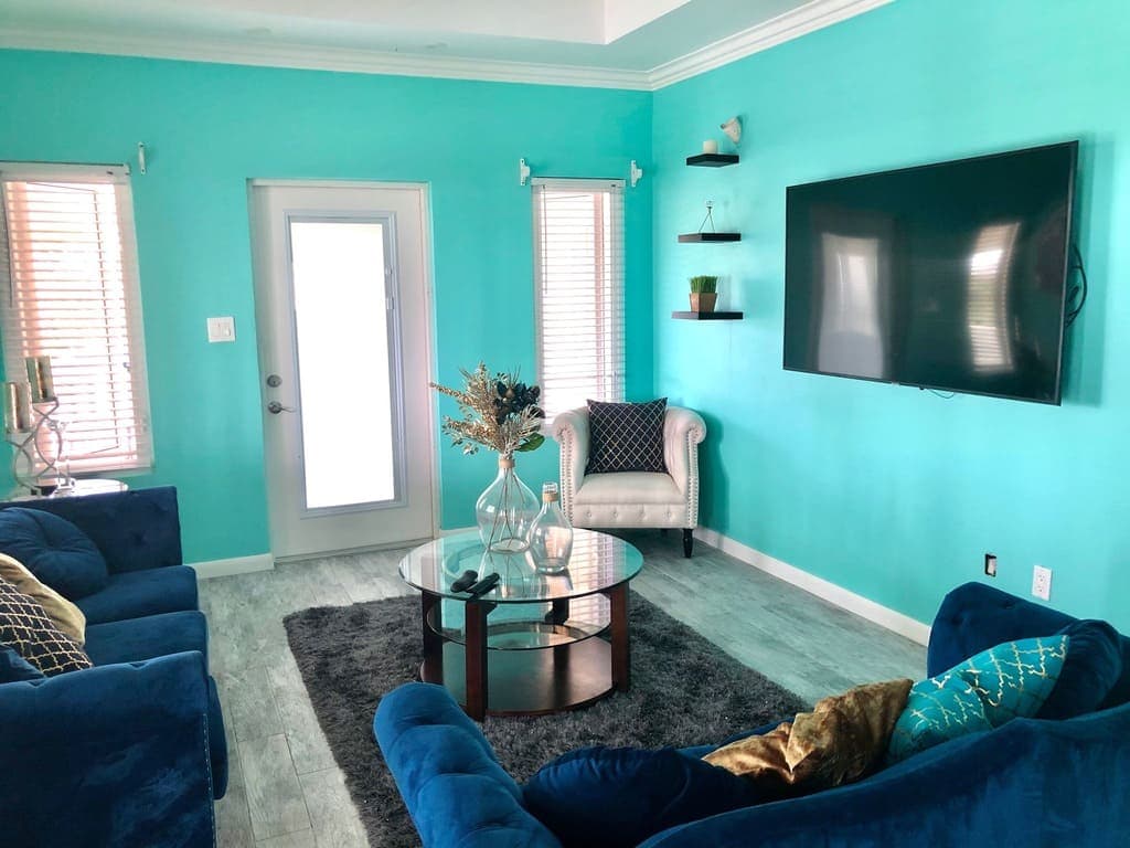 Bright turquoise living room with modern decor and stylish furniture, featuring a wall-mounted TV, cozy blue sofas, and decorative accents, ideal for home staging by 17 Degrees North Realtors.