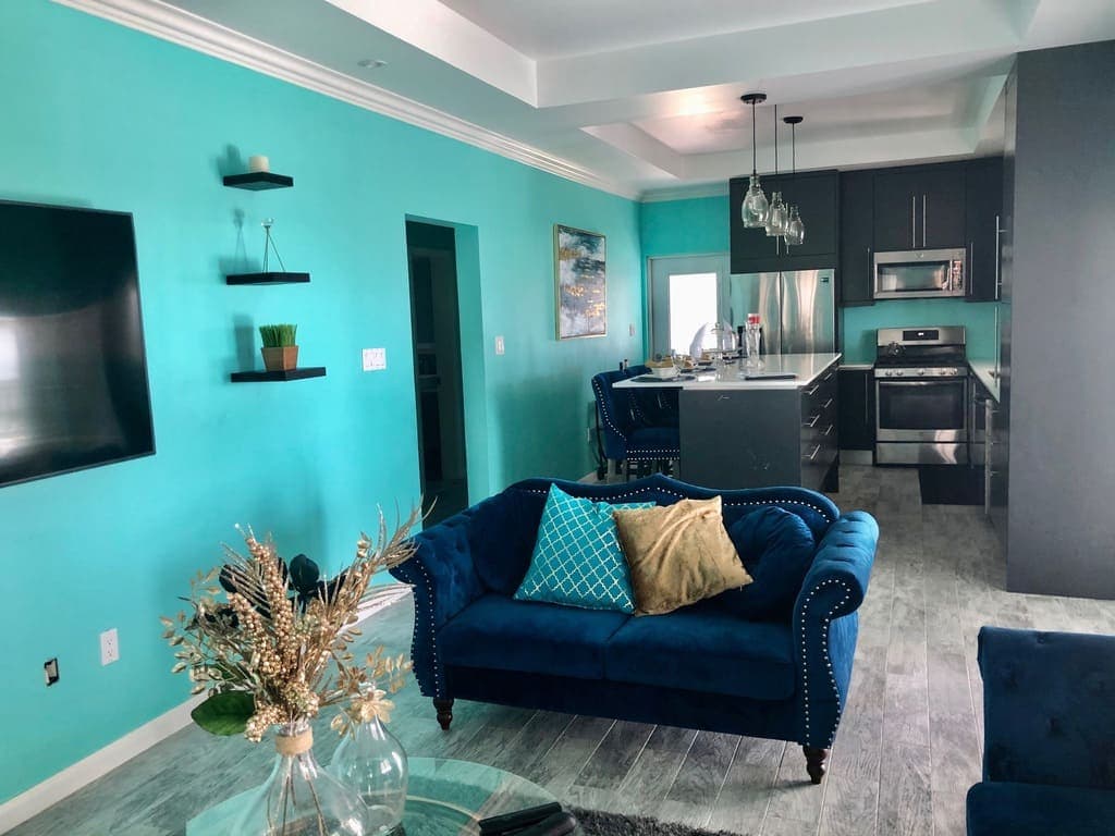 Bright turquoise wall décor in modern living room featuring navy velvet sofa and open-concept kitchen with stainless steel appliances, ideal for real estate listings in Nevís.