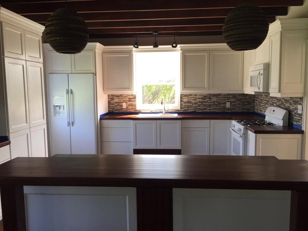 IMG_9003 Bright modern kitchen with white cabinets, dark wooden countertops, mosaic backsplash, and large window in Nevu00eds, featuring stainless steel appliances and high-quality finishes.