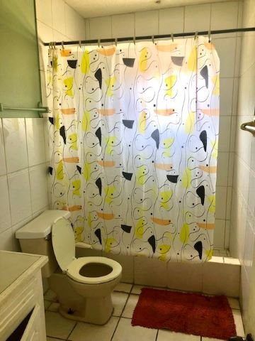 Bright bathroom with colorful floral shower curtain, white tile walls, and a toilet, ideal for a cozy home living space.