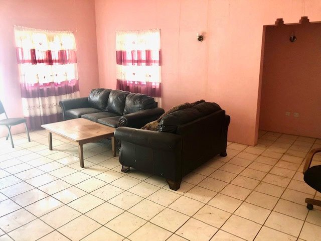 Gray leather sofas arranged around a wooden coffee table in a cozy living room with pink walls and tiled flooring.