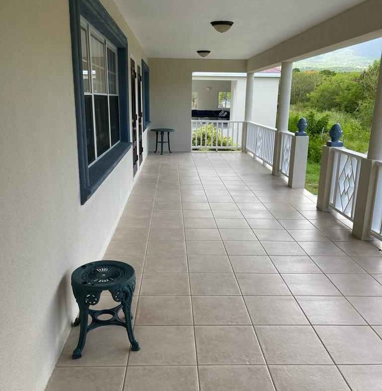 Spacious covered front porch with beige tile flooring, white railings, and lush green backyard views, ideal for relaxing and outdoor entertaining in a 17 Degrees North property.