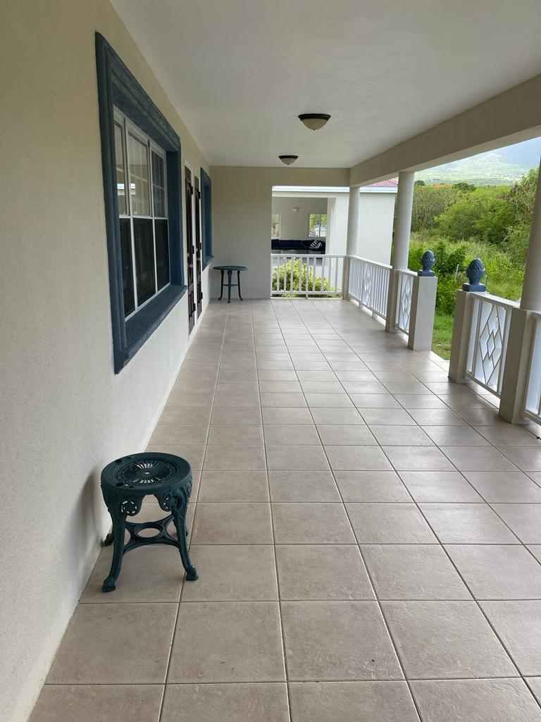 Spacious covered front porch with beige tile flooring, white railings, and lush green backyard views, ideal for relaxing and outdoor entertaining in a 17 Degrees North property.