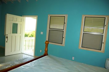 Bright blue bedroom interior with open door and window shutters, showcasing a cozy living space in a tropical or coastal property.