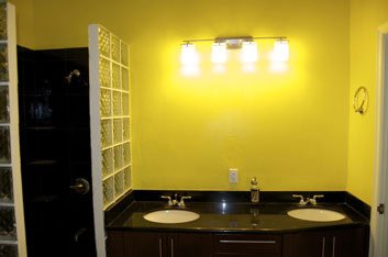 Modern bathroom vanity with double sinks, black countertop, yellow painted walls, and bright lighting - ideal for home renovation or real estate listings.