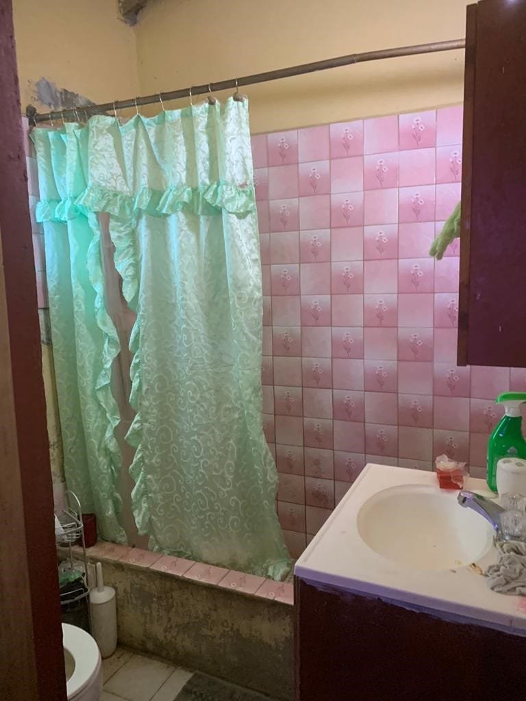 BN22 Molyneux Housing Development 6 Vintage bathroom with pink tiled walls, green floral shower curtain, and basic fixtures, offering affordable housing options or potential renovation project.