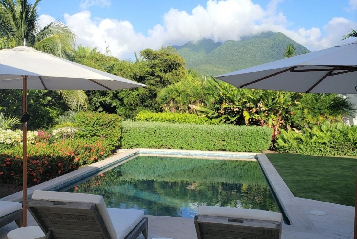 Luxury poolside villa in Nevis with mountain views, outdoor lounging area, lush landscaping, and tropical surroundings – perfect for Caribbean real estate and vacation homes.