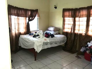 - Small bedroom with brown curtains and a messy bed featuring clothes and pillows, located in a real estate listing by 17 Degrees North Realtors.