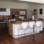 Modern kitchen with white cabinets, colorful tile backsplash, and a breakfast bar with four white chairs, perfect for homebuyers seeking contemporary real estate in Evnis.