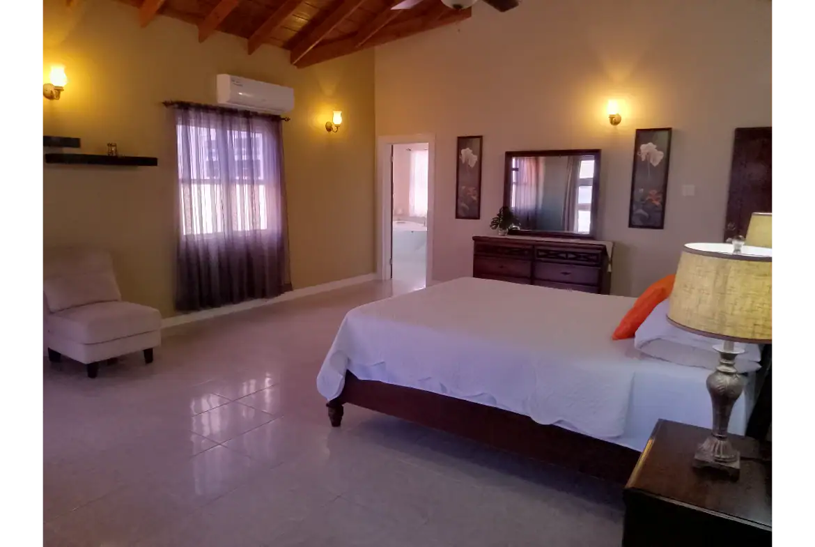 Spacious bedroom with high vaulted ceilings, modern decor, and comfortable furnishings at 17 Degrees North Realtors in Nevis. Perfect for luxury real estate buyers.