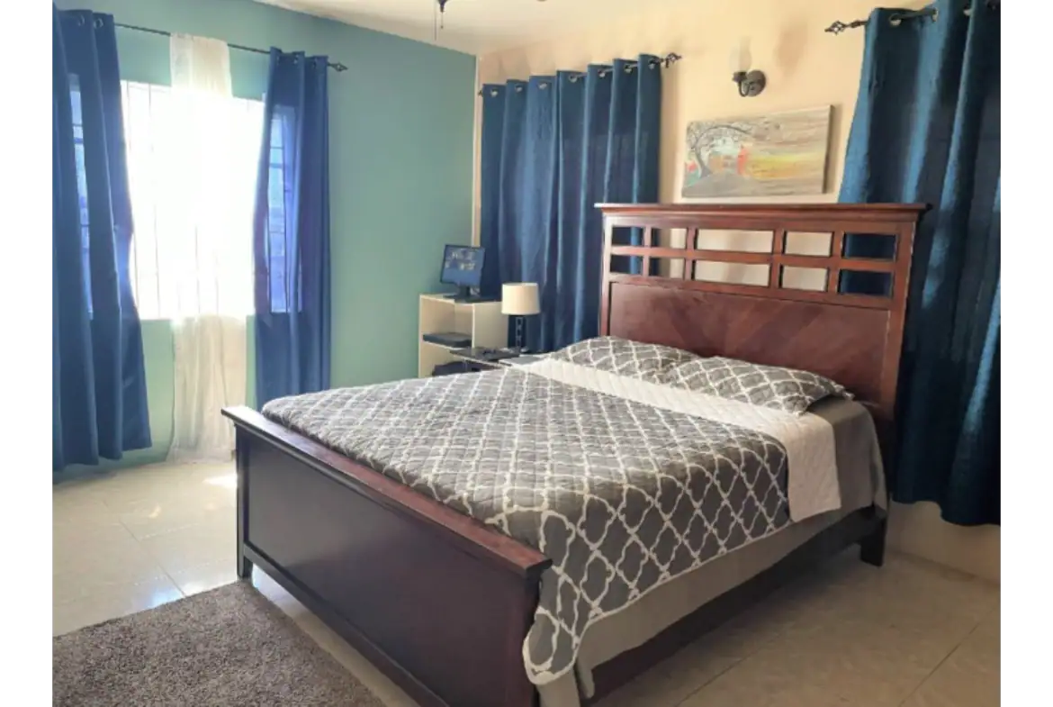 Cozy bedroom with large window, blue curtains, and wooden bed frame, ideal for vacation rentals near 17 Degrees North. Perfect for relaxing stays in Evian.