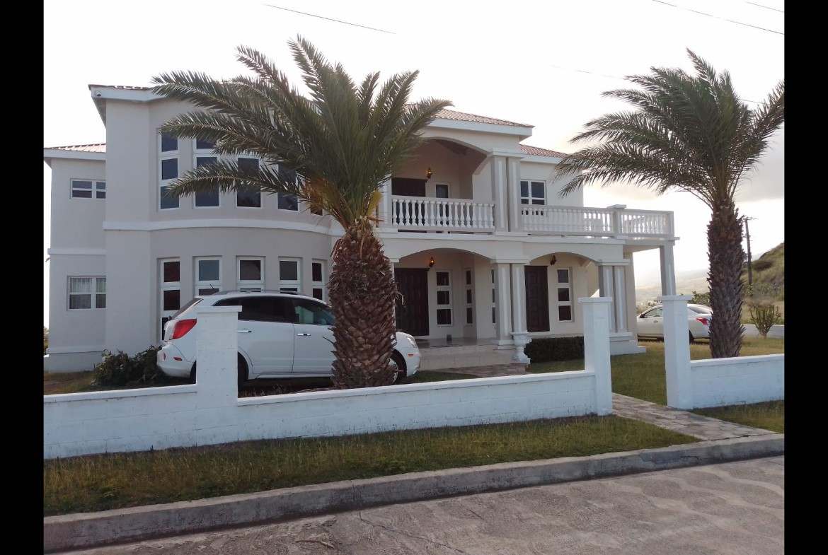 Luxurious beachfront property with modern architecture, palm trees, and ample parking, available through 17 Degrees North Realtors. Perfect for buyers seeking upscale homes in a coastal area.