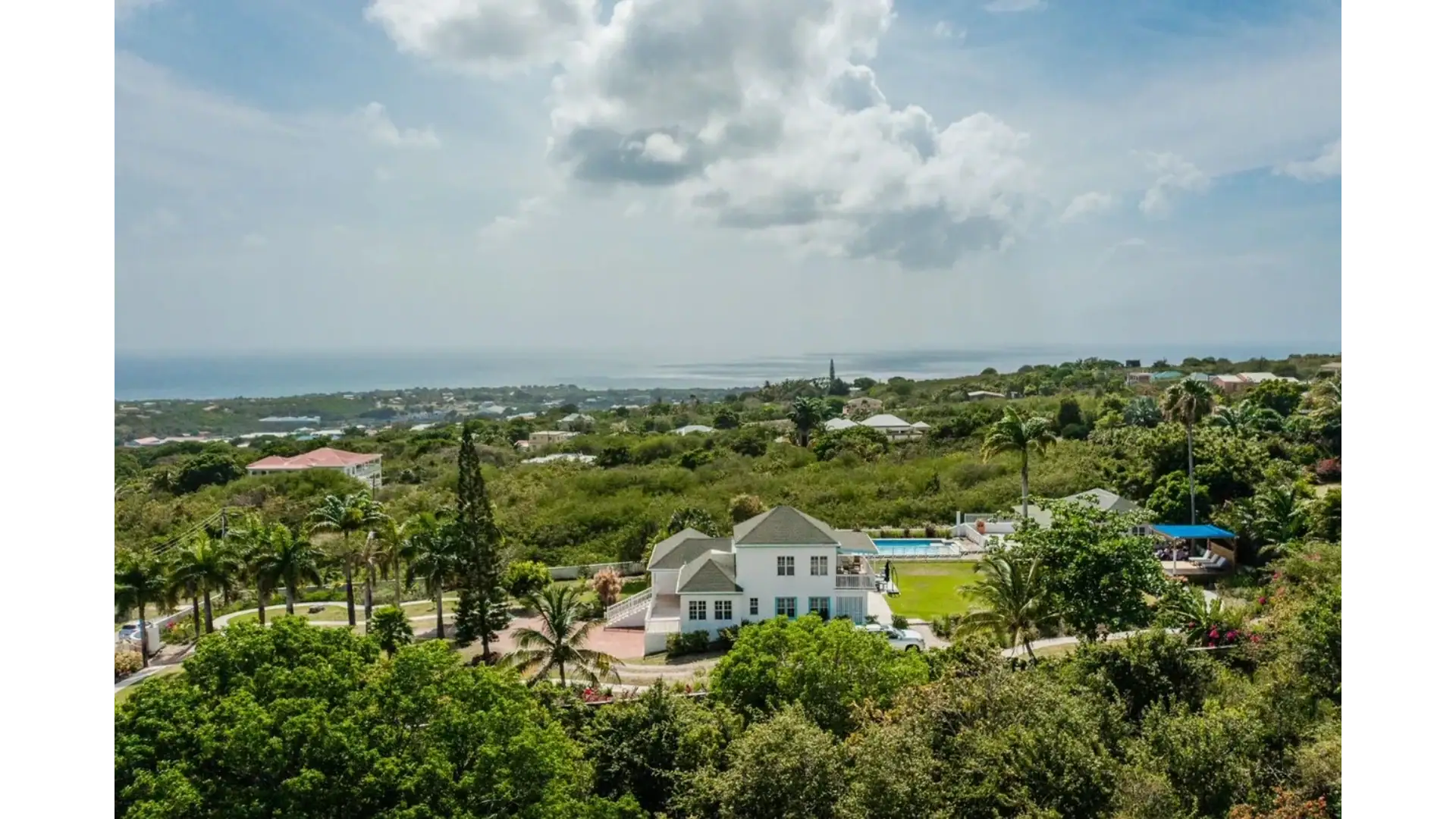Luxurious ocean-view home surrounded by lush greenery with palm trees, beautiful gardens, and a private pool in a tropical estate. Perfect for relaxing and enjoying the scenic landscape.