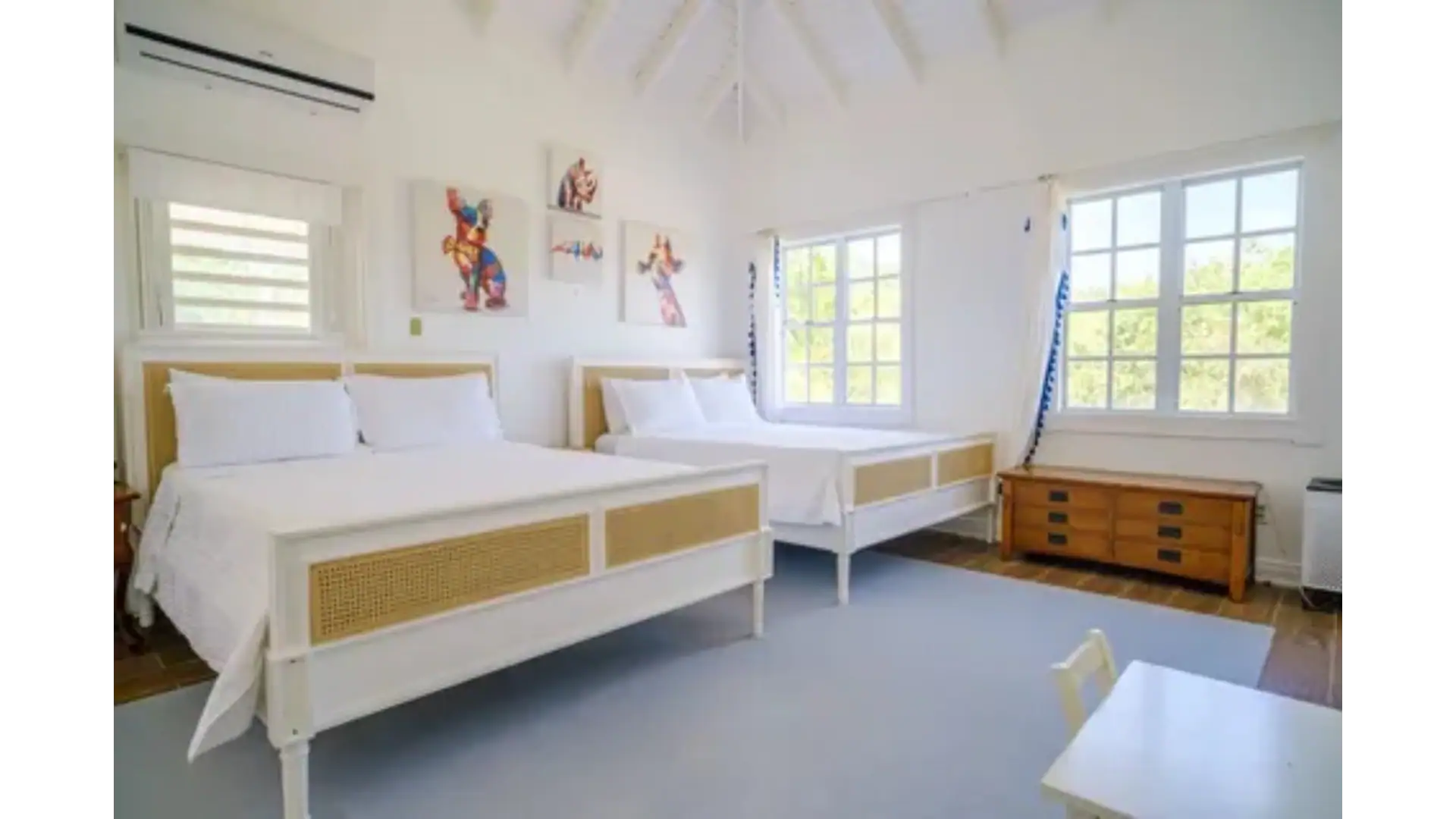 Bright and airy bedroom featuring two white beds, stylish artwork, and large windows with ocean views, perfect for luxury real estate in Nevis.
