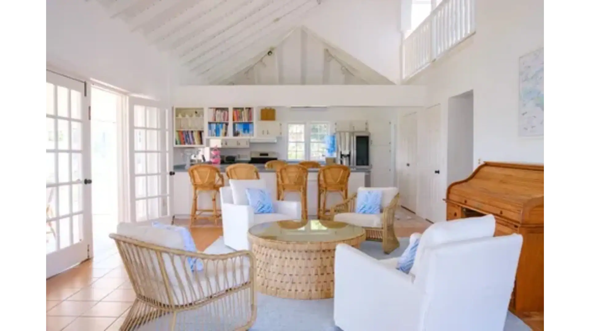 Spacious beach house living room with white walls, vaulted ceiling, and ample natural light, featuring cozy white and wicker furniture, perfect for Caribbean vacation rentals or coastal home retreats.