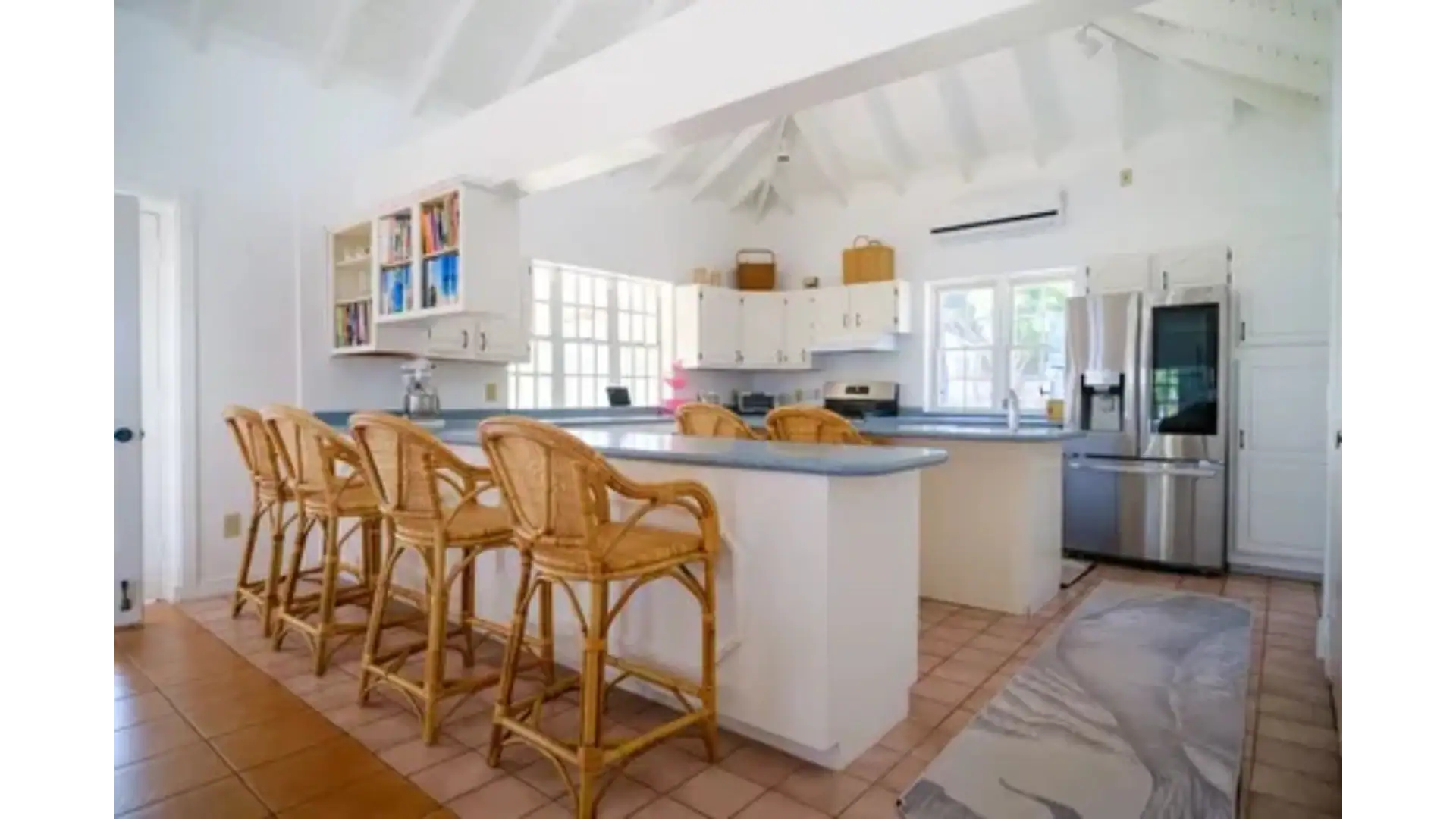 Bright, airy kitchen in a beachfront home with white cabinetry, stainless steel appliances, and a spacious island with wooden bar stools, perfect for coastal living.