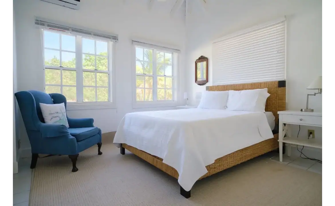 Bright and airy bedroom at 17 Degrees North Realtors, featuring large windows, white walls, and coastal-inspired decor, perfect for relaxing with a tropical view.