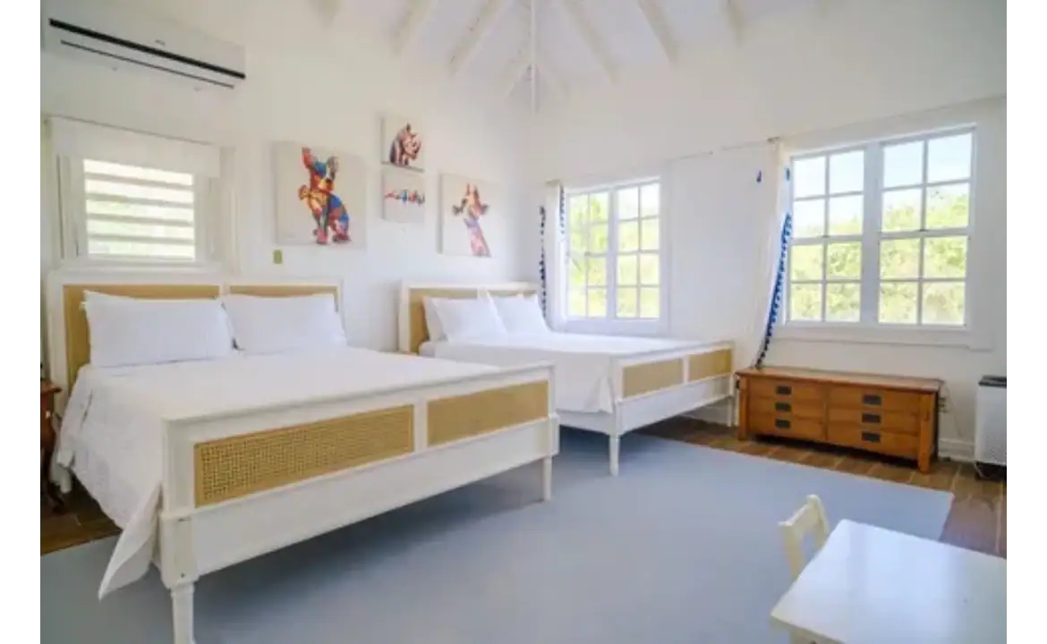 Bright and airy bedroom featuring two white beds, stylish artwork, and large windows with ocean views, perfect for luxury real estate in Nevis.