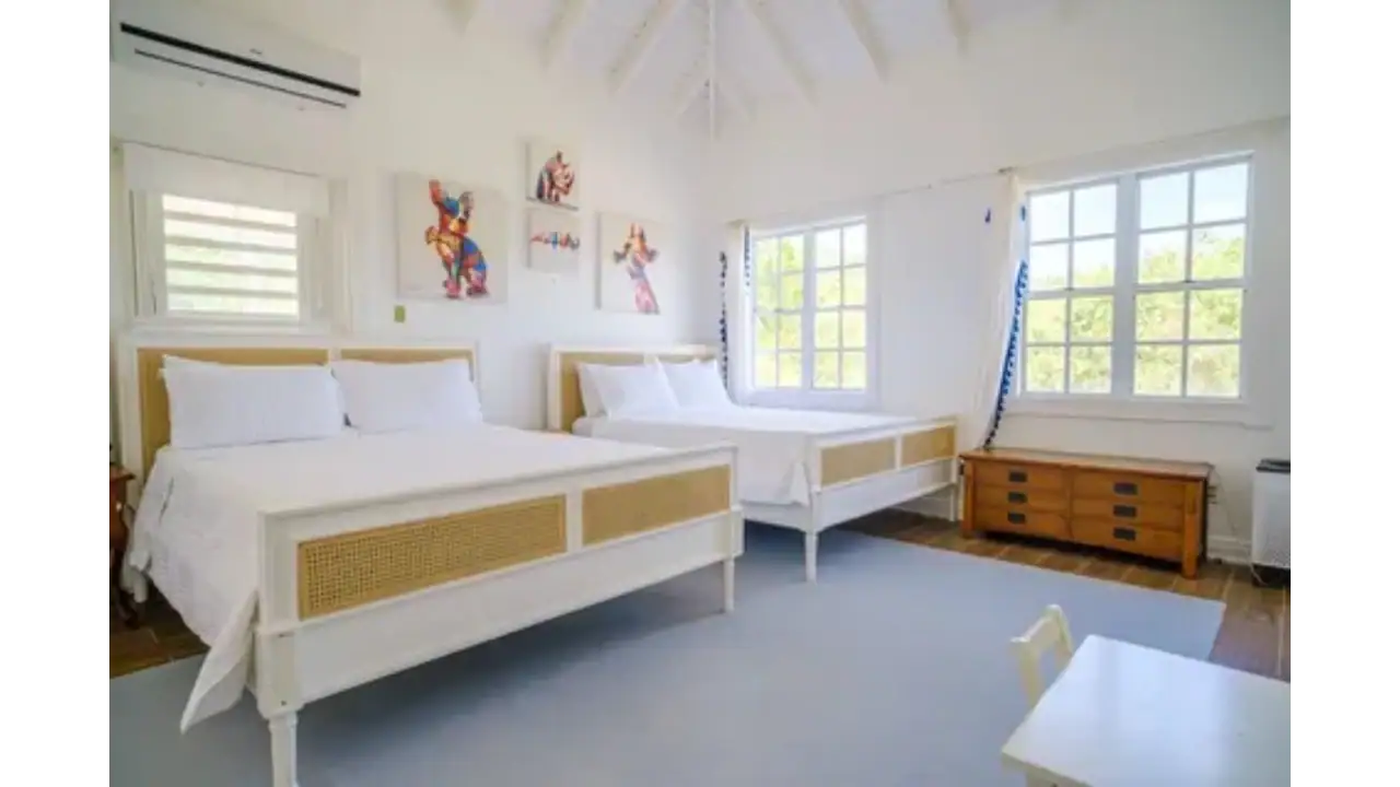 Bright and airy bedroom featuring two white beds, stylish artwork, and large windows with ocean views, perfect for luxury real estate in Nevis.