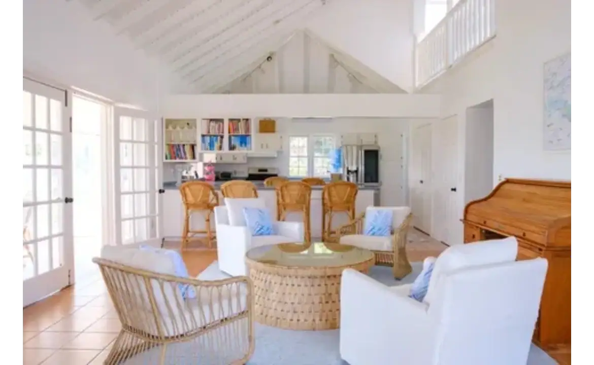 Spacious beach house living room with white walls, vaulted ceiling, and ample natural light, featuring cozy white and wicker furniture, perfect for Caribbean vacation rentals or coastal home retreats.