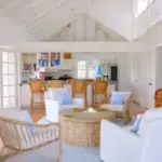 Spacious beach house living room with white walls, vaulted ceiling, and ample natural light, featuring cozy white and wicker furniture, perfect for Caribbean vacation rentals or coastal home retreats.