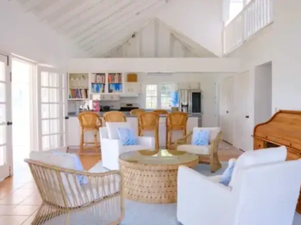 Spacious beach house living room with white walls, vaulted ceiling, and ample natural light, featuring cozy white and wicker furniture, perfect for Caribbean vacation rentals or coastal home retreats.