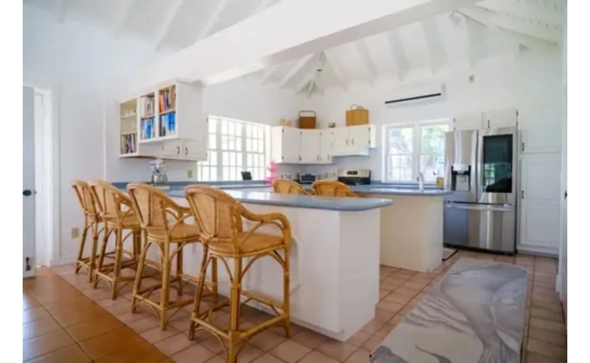 Bright, airy kitchen in a beachfront home with white cabinetry, stainless steel appliances, and a spacious island with wooden bar stools, perfect for coastal living.