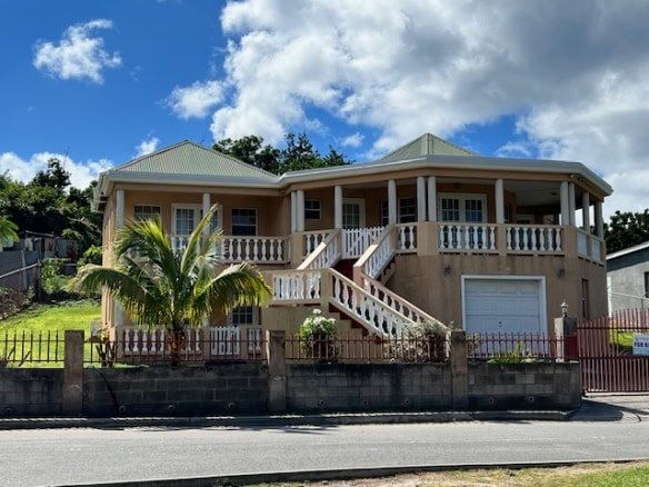 17 Degrees North Realtors luxury home with a vibrant tropical front yard, spacious balcony, and modern architecture located in Nevis. Perfect for real estate investment and island living.