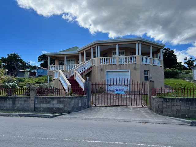 17 Degrees North Realtors property for rent, showcasing a spacious elevated house with a balcony, garage, and beautiful landscaping in a serene neighborhood.