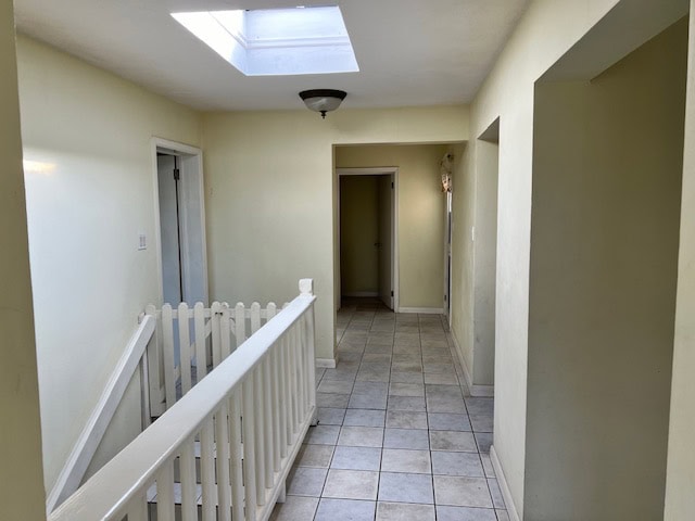 Bright hallway with natural skylight, beige walls, tiled flooring, and staircase in a modern home for real estate in Evvis.