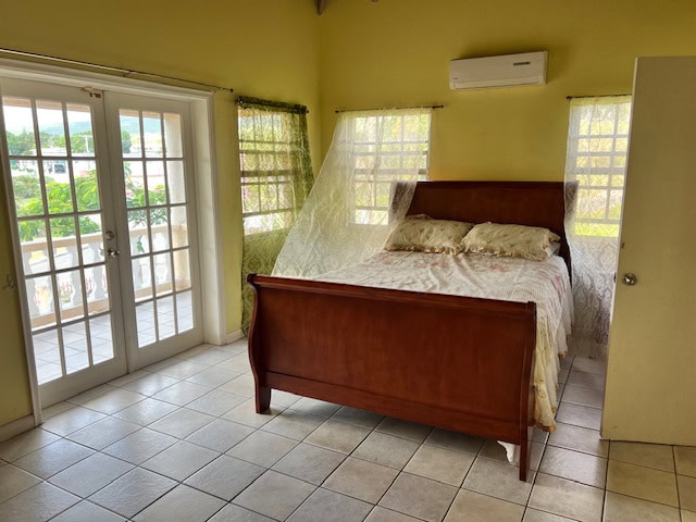 Spacious bedroom with balcony access, large windows, and natural light, featuring a wooden bed frame, yellow walls, and tile flooring, ideal for homebuyers seeking comfortable living spaces in Evista.